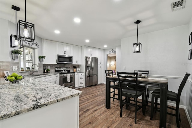 kitchen with appliances with stainless steel finishes, light stone countertops, decorative light fixtures, sink, and white cabinetry