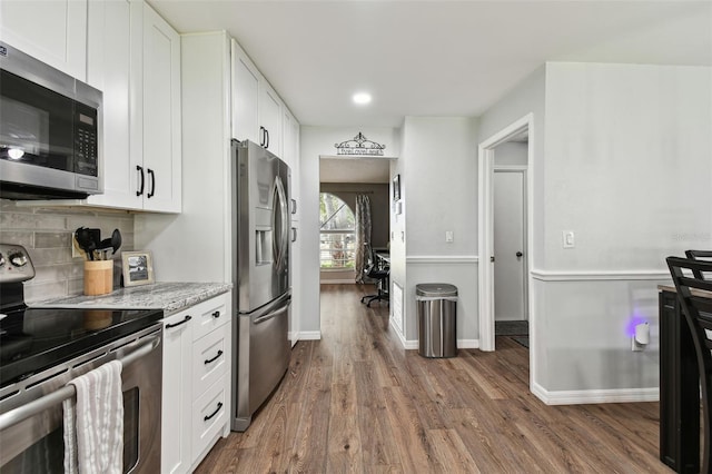 kitchen with white cabinetry, hardwood / wood-style flooring, stainless steel appliances, light stone countertops, and decorative backsplash