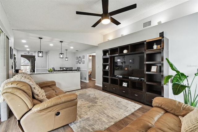 living room with light wood-type flooring, vaulted ceiling, ceiling fan, and a textured ceiling