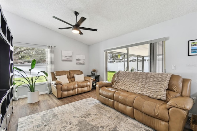 living room with ceiling fan, lofted ceiling, a textured ceiling, and light hardwood / wood-style flooring