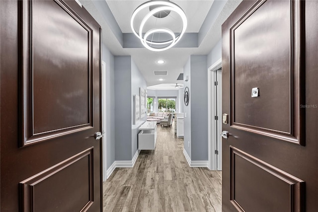 hall with light wood-style flooring, visible vents, baseboards, and a raised ceiling