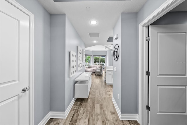 hall with light wood-style floors, baseboards, a textured ceiling, and recessed lighting