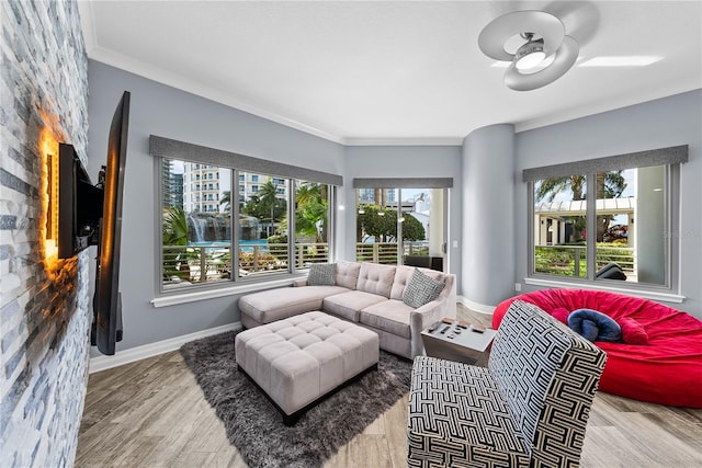 living area with baseboards, ceiling fan, wood finished floors, and crown molding