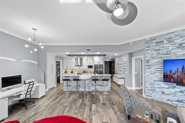 interior space with a breakfast bar, tasteful backsplash, stainless steel fridge with ice dispenser, ornamental molding, and wall chimney exhaust hood