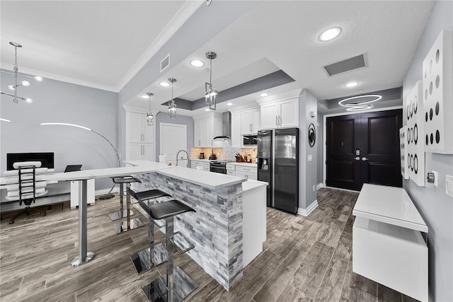 kitchen with wall chimney exhaust hood, a breakfast bar area, wood finished floors, fridge with ice dispenser, and white cabinetry