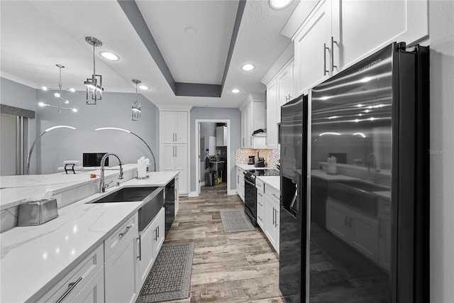 kitchen with light stone counters, white cabinetry, a sink, and black appliances