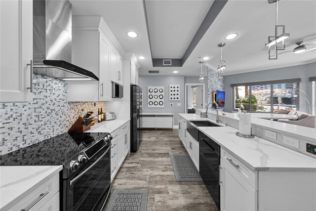 kitchen with a sink, white cabinets, wall chimney exhaust hood, black appliances, and tasteful backsplash