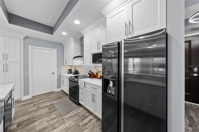 kitchen featuring light countertops, black refrigerator with ice dispenser, decorative backsplash, double oven range, and wall chimney exhaust hood