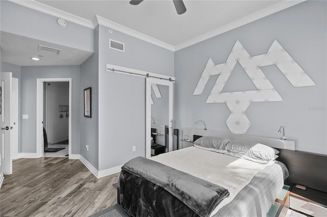 bedroom with visible vents, a barn door, ornamental molding, wood finished floors, and baseboards