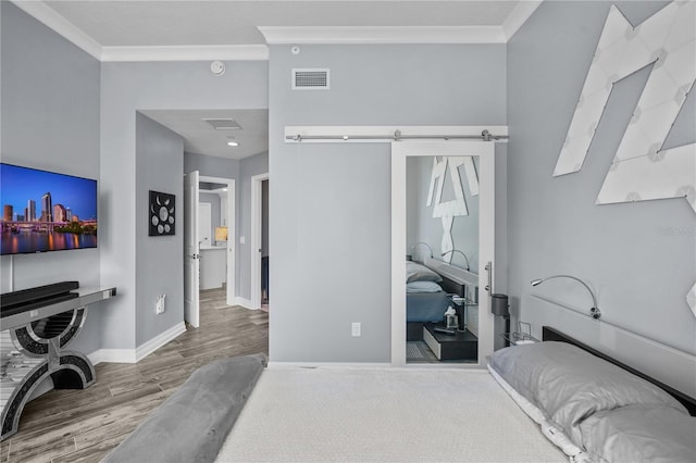 bedroom with a barn door, wood finished floors, visible vents, baseboards, and crown molding