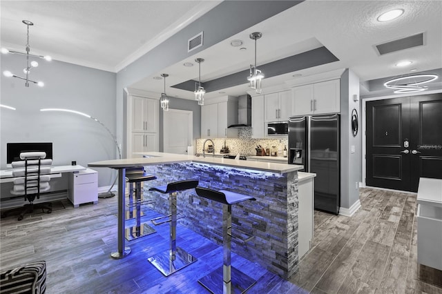 kitchen featuring wall chimney range hood, visible vents, fridge with ice dispenser, and built in microwave