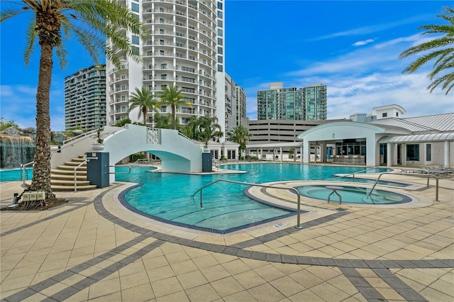 pool featuring a community hot tub, a city view, a patio, and stairs