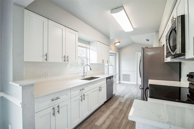 kitchen featuring appliances with stainless steel finishes, white cabinetry, a sink, and light stone counters