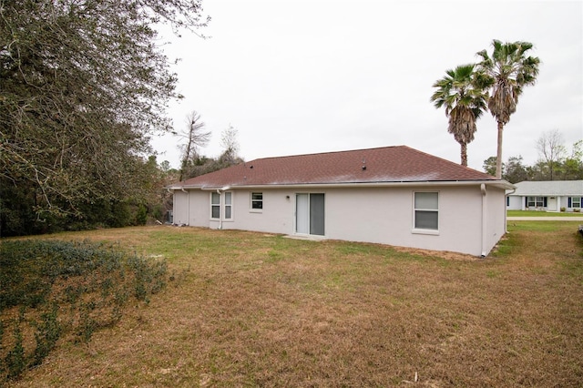 rear view of property featuring a lawn and stucco siding