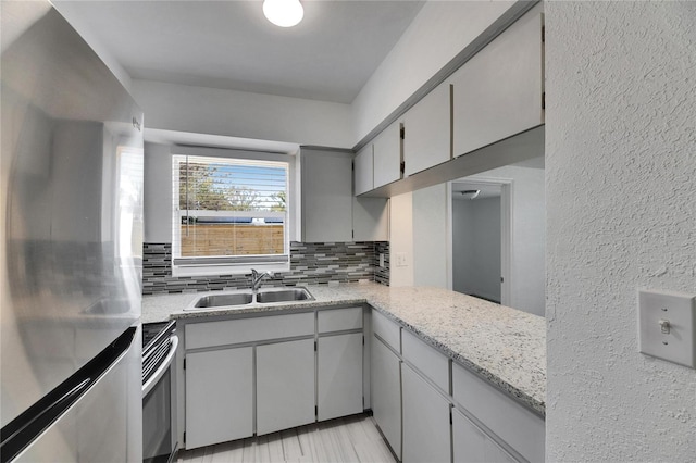 kitchen with appliances with stainless steel finishes, sink, kitchen peninsula, gray cabinets, and tasteful backsplash