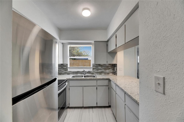 kitchen featuring gray cabinetry, sink, backsplash, light stone counters, and appliances with stainless steel finishes