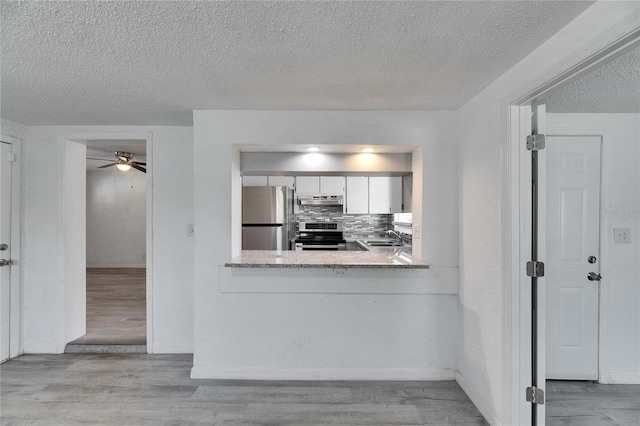 kitchen with white cabinets, light hardwood / wood-style floors, appliances with stainless steel finishes, and decorative backsplash