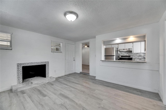 unfurnished living room featuring ceiling fan, a tile fireplace, a textured ceiling, and light wood-type flooring