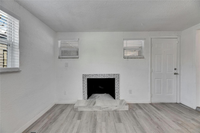 unfurnished living room featuring a fireplace, light hardwood / wood-style floors, and a textured ceiling