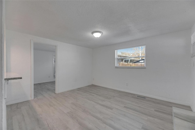 spare room featuring light wood-type flooring and a textured ceiling