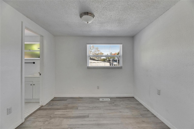 spare room featuring light wood-type flooring and a textured ceiling