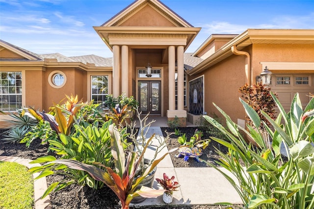 view of exterior entry with stucco siding, french doors, and a garage