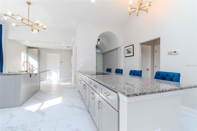 kitchen with black electric stovetop, marble finish floor, an inviting chandelier, and a kitchen island with sink