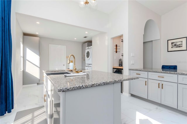 kitchen with a kitchen island with sink, stacked washer / drying machine, recessed lighting, marble finish floor, and light stone counters