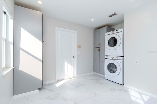 laundry room featuring visible vents, marble finish floor, stacked washer and clothes dryer, baseboards, and cabinet space