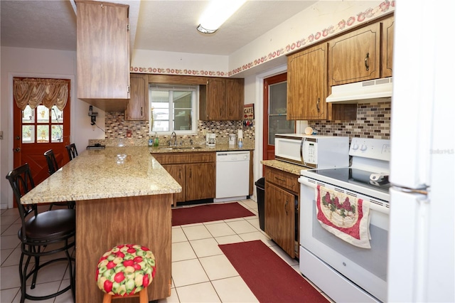 kitchen with white appliances, brown cabinets, a kitchen breakfast bar, a peninsula, and under cabinet range hood