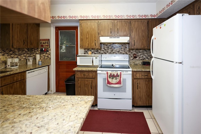 kitchen with white appliances, light tile patterned floors, decorative backsplash, light stone counters, and under cabinet range hood