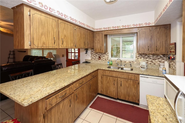 kitchen with brown cabinets, dishwasher, a peninsula, and a sink