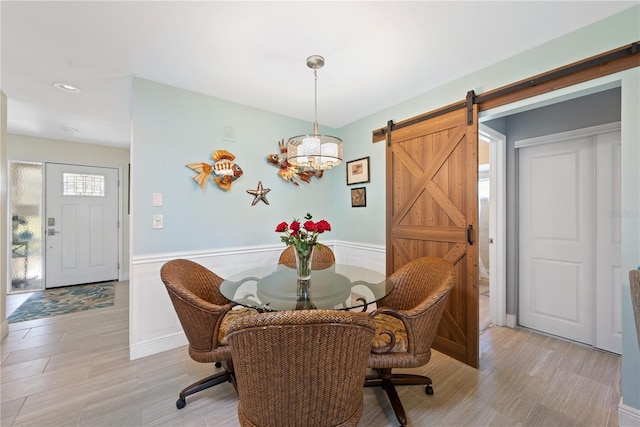 dining space featuring light wood-type flooring, a wainscoted wall, and a barn door