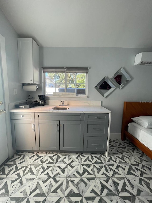 kitchen with a wall mounted air conditioner, light countertops, gray cabinetry, light floors, and a sink