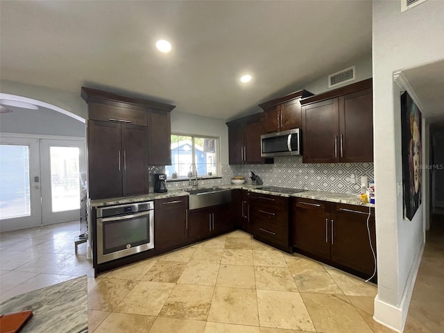 kitchen with stainless steel appliances, a sink, visible vents, dark brown cabinets, and decorative backsplash