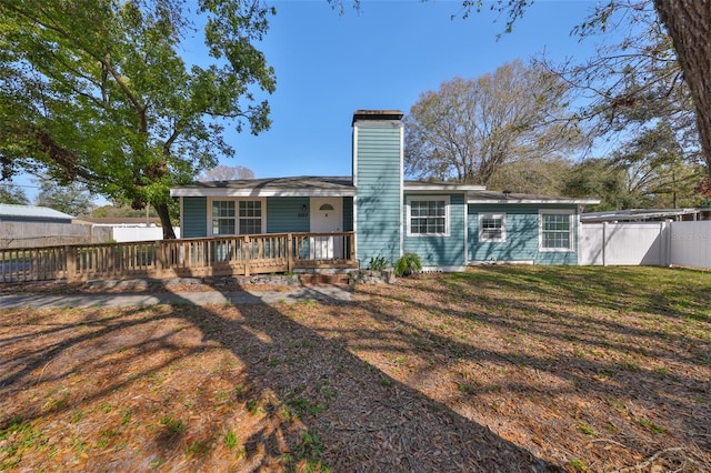 back of property with a deck, a fenced backyard, a lawn, and a chimney