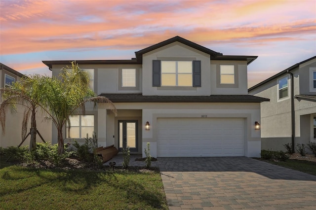 view of front of property with decorative driveway, a lawn, an attached garage, and stucco siding