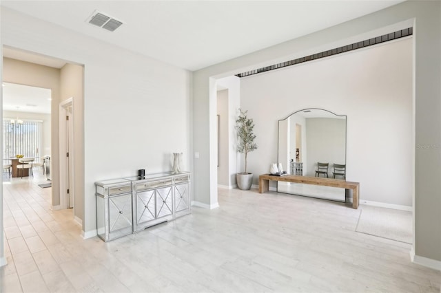 corridor featuring light wood-style flooring, visible vents, a chandelier, and baseboards