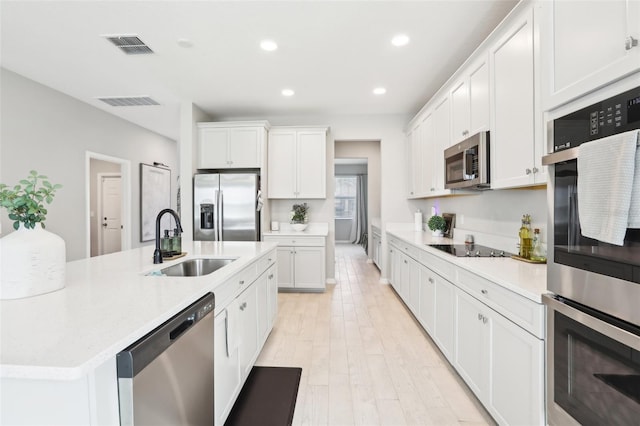 kitchen with a kitchen island with sink, stainless steel appliances, a sink, white cabinetry, and light countertops