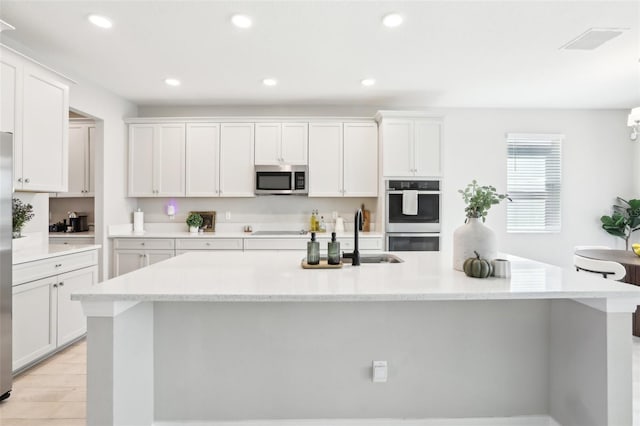 kitchen with stainless steel appliances, white cabinets, a sink, and an island with sink