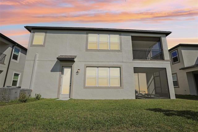 back of property with a balcony, central AC, a lawn, and stucco siding