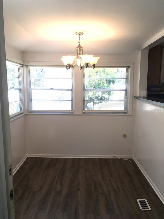 unfurnished dining area with dark wood-type flooring, a chandelier, visible vents, and baseboards