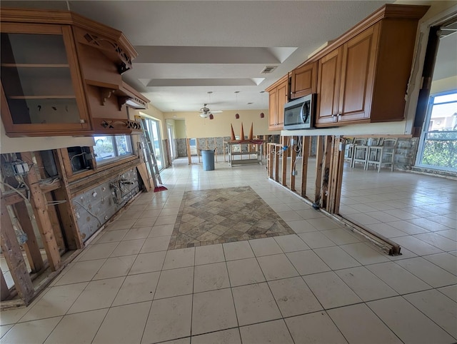 kitchen with visible vents, brown cabinetry, glass insert cabinets, stainless steel microwave, and open shelves