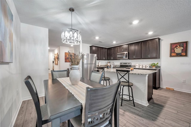 dining space featuring a notable chandelier, light hardwood / wood-style flooring, and a textured ceiling