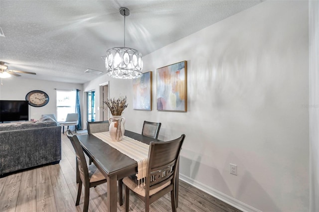 dining area featuring hardwood / wood-style flooring, a textured ceiling, and ceiling fan with notable chandelier