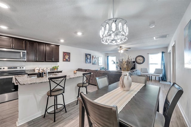 dining room with light wood-type flooring, a textured ceiling, and ceiling fan