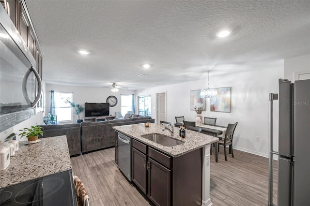 kitchen with light wood-type flooring, a center island with sink, sink, light stone counters, and appliances with stainless steel finishes