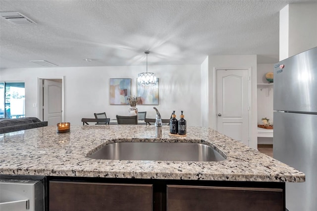 kitchen with a textured ceiling, sink, light stone countertops, and stainless steel fridge