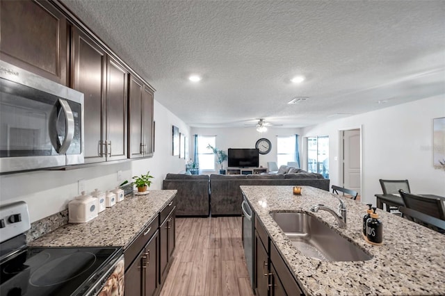 kitchen with appliances with stainless steel finishes, sink, dark brown cabinetry, and light stone countertops