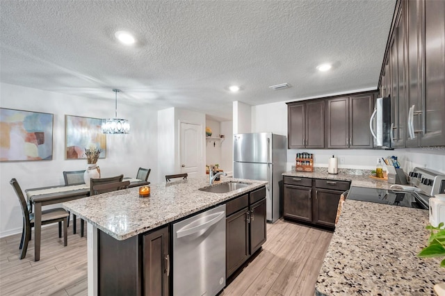 kitchen featuring appliances with stainless steel finishes, light hardwood / wood-style flooring, a center island with sink, pendant lighting, and sink